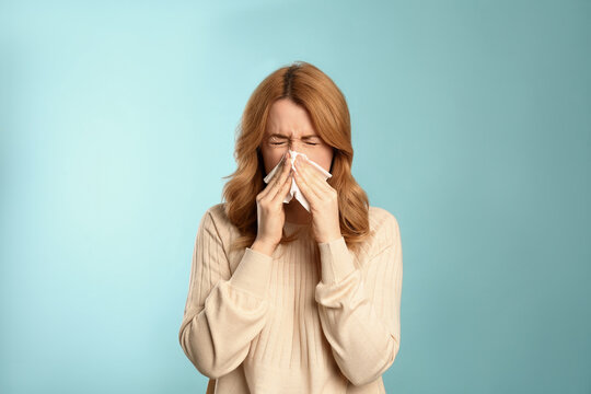 Woman with tissue suffering from runny nose on light blue background