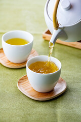 Cups of green tea and teapot.
Pouring fresh green tea in the cups.
