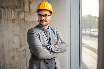 Successful architect standing in building in construction process with arms crossed and looking...