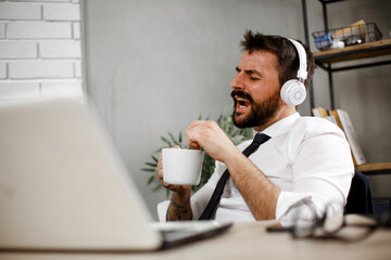 Attractive businessman in office. Young businessman with headphones singing at work