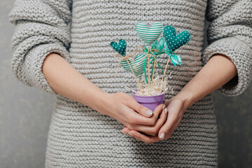 A girl holds a pot of homemade green hearts on wooden sticks. Heart shaped flowers concept.