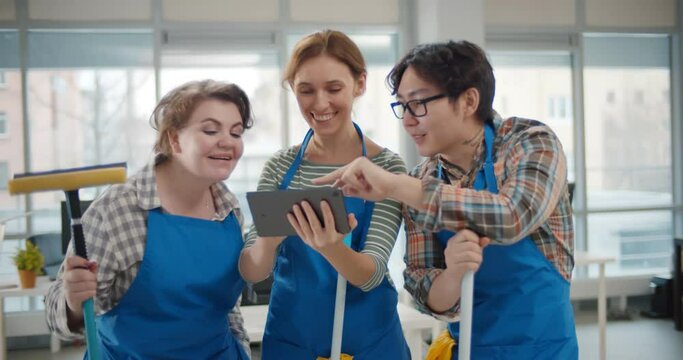 Professional janitors in aprons using tablet pc working in office