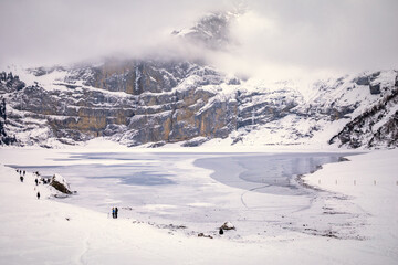 Fototapeta na wymiar People spending day by frozen lake in snowy mountain landscape
