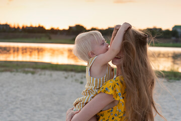 Little girl playing with moms hair. Portrait in motion mother and child on river and sunset...