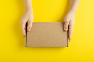 Cardboard box in child hands on yellow background, top view. Copy space. Mock up.