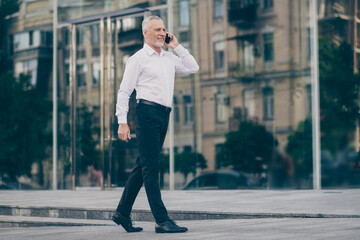 Photo of cute attractive mature worker man wear formal shirt walking talking modern device outdoors city street