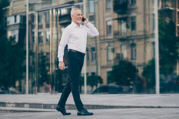 Fototapeta premium Photo of cute attractive mature worker man wear formal shirt walking talking modern device outdoors city street