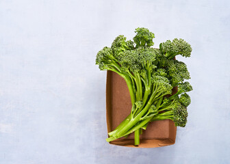 Raw broccolini, fresh organic broccoli florets green vegetable baby broccoli in paper box for storing food Plastic-free packaging, zero west concept. Light blue background with copy space.