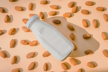 Bottle of almond milk and almond kernels are placed on a colored paper background with space for text. 