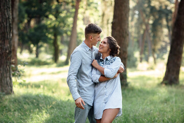 Fototapeta premium Cheerful young woman and man are hugging outdoors in summer park. Dating and romantic vacation. couple in love gently looking at each other on sunny day. Love and relationships between young people