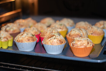 Muffins with dried fruits are baked in the oven in multi-colored silicone molds. Close-up of baked goods in the oven. Place for an inscription.
