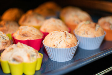 Muffins with dried fruits are baked in the oven in multi-colored silicone molds. Close-up of baked goods in the oven. Place for an inscription.