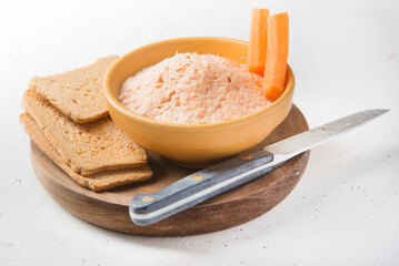 Smoked salmon and soft cheese spread pate with brown bread and carrot on white background.