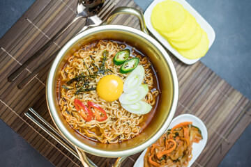 Korean traditional Ramyeon noodle  with egg yolk, chilli, kimchi in a traditional korean noodle pot, Spicy Korean Ramyeon instant noodle a traditional dish.