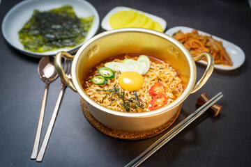 Korean traditional Ramyeon noodle  with egg yolk, chilli, kimchi in a traditional korean noodle pot, Spicy Korean Ramyeon instant noodle a traditional dish.