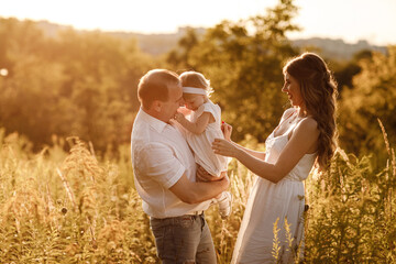 Family, parenthood, leisure and people concept - happy mother, father and little daughter playing in summer park. Young family spending time together on vacation, outdoors.