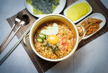 Korean style instant noodle, Ramyeon with egg yolk, chilli, kimchi vegetables pickled and radish pickles in a traditional korean noodle pot.