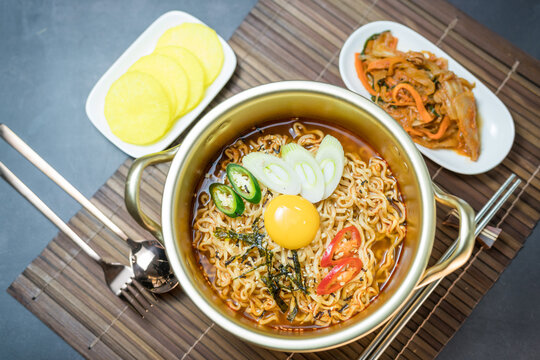 Korean style instant noodle, Ramyeon with egg yolk, chilli, kimchi vegetables pickled and radish pickles in a traditional korean noodle pot.