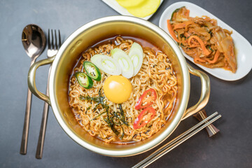 Korean style instant noodle, Ramyeon with egg yolk, chilli, kimchi vegetables pickled and radish pickles in a traditional korean noodle pot.