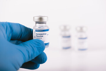 Hand with blue latex glove holding covid vaccine vial