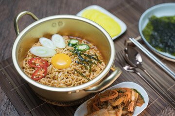 Korean style instant noodle, Ramyeon with egg yolk, chilli, kimchi vegetables pickled and radish pickles in a traditional korean noodle pot.