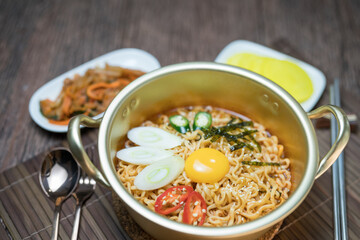 Korean style instant noodle, Ramyeon with egg yolk, chilli, kimchi vegetables pickled and radish pickles in a traditional korean noodle pot.