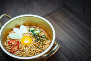 Korean style instant noodle, Ramyeon with Egg yolk, Chilli, Seaweed and Bunching Onion  in a traditional korean noodle pot.