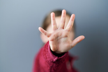 Kind in rotem Pullover zeigt fünf Finger und hält die Hand vor das Gesicht.