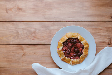 Delicious freshly baked vegan strawberry and cherry galette on wooden rustic background, top view. Sweet food, summer dessert.