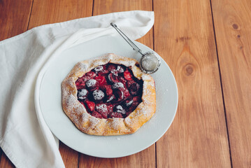 Delicious freshly baked vegan strawberry and cherry galette on wooden rustic background. Sweet food, summer dessert. Copy space.