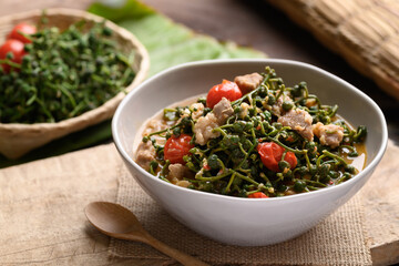 Northern Thai food (Kaeng Sa Lae), Spicy soup Broussonetia Kurzii with pork and tomatoes in a bowl on wooden background, Seasonal food in North Thailand