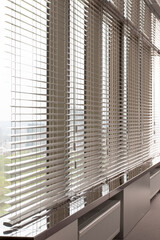 Aluminum blinds. Made from metal. Venetian blinds closeup on the window. Silver color. City landscape is in the background.