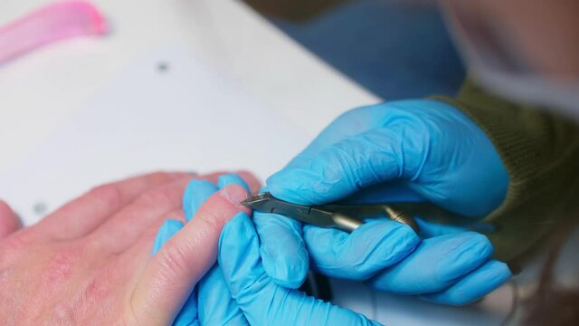 Manicurist uses metal nippers to remove dry skin of cuticle around nails. Processe of manicure.