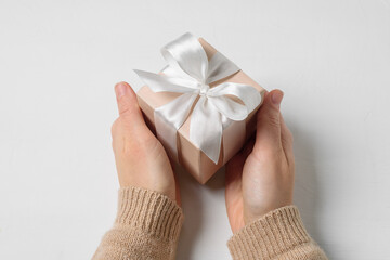 Beige gift box with white bow in woman hands on white background