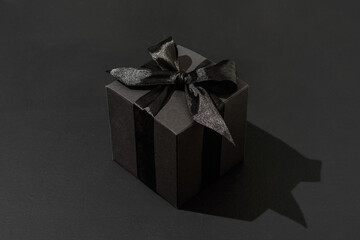 Black gift box with bow on black background. Hard light