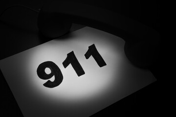 Call 911 and emergency call concept, text 911 on paper and phone isolated on black.