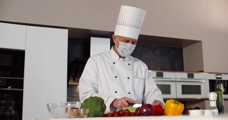 Senior male chef wearing safety mask cooking in modern kitchen