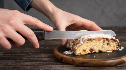 hands of the chef slicing a Stollen cake with a knife at kitchen. Stollen coated with powdered sugar