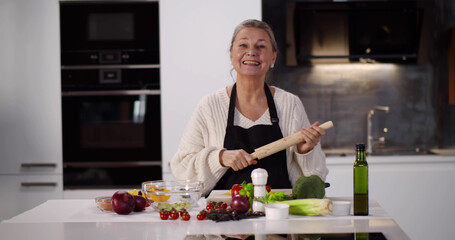 Senior woman smiling holding rolling pin while cooking in kitchen