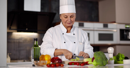 Portrait of senior woman chef cutting vegetables in modern kitchen