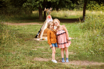 Cute sisters posing next to wigwam decoration, spending time outdoor in summer. © Natalia