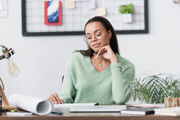 thoughtful african american interior designer sitting at desk at home studio, blurred foreground