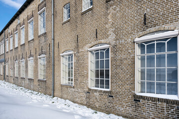Rear facade of the former Nooitgedagt ice skating and woodworking tools factory in IJlst, Friesland in winter with snow, sun and blue sky in the Netherlands