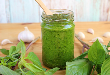 Fresh Homemade Basil Pesto Sauce in Glass Bottle with Its Ingredients on Wooden Table	