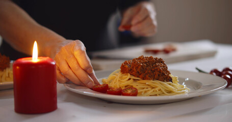 Close up of woman decorating pasta with cherry tomato preparing romantic dinner