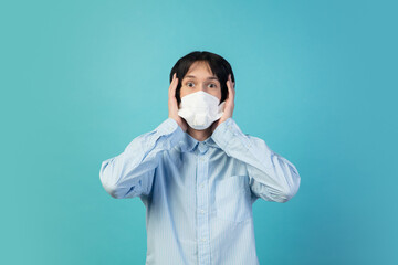 Shocked, scared. Man in protective face mask isolated on blue studio background. New rules of COVID spreading prevention. Copyspace for ad. Pandemic, healthcare and medicine, coronavirus concept