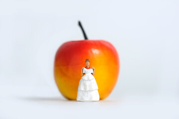 Diet plan before wedding or marriage day concept. Woman standing in front of apple with trying wedding dress. Miniature people, toys photography.