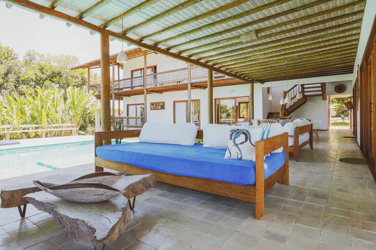 Modern summer holiday or vacation wooden beach house pool area interior with two sofas and rustic decoration. Plants and nature outside the terrace.