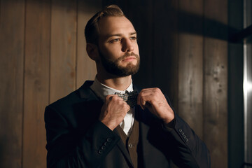 Majestic handsome man with a beard, dressed in a classic suit and bow tie. The man straightens his bow tie and preps up. A successful businessman is preparing for a meeting with clients - Powered by Adobe
