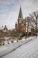 Fototapeta na wymiar Snow white winter wonderland with pointy rooftop tower with cants of Drogenapstoren part of historic city center of medieval Hanseatic town during a snowstorm